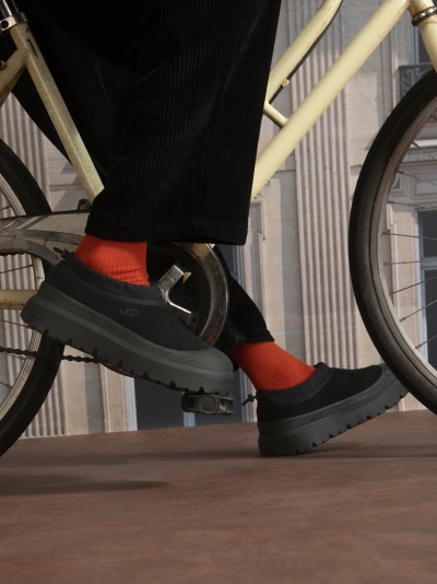Cyclist in black pants, orange socks, black UGG slip-on shoes on bicycle pedals.