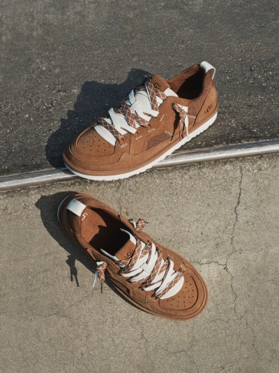 Light beige suede sneaker on a two-tone concrete surface with UGG branding.
