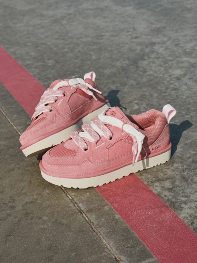 Pair of pink UGG sneakers with white laces on concrete, a faded red stripe.